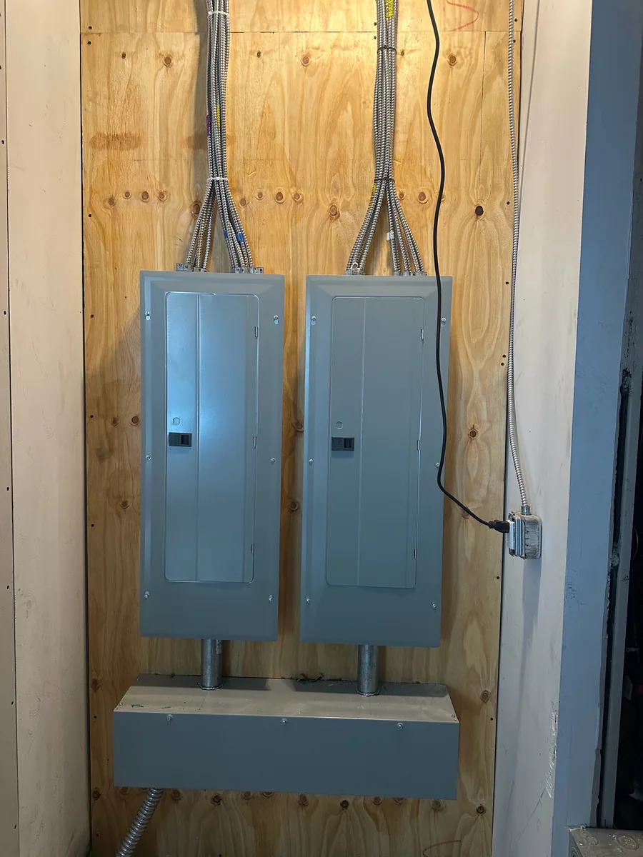 Two new side-by-side electrical panels mounted on a plywood backboard